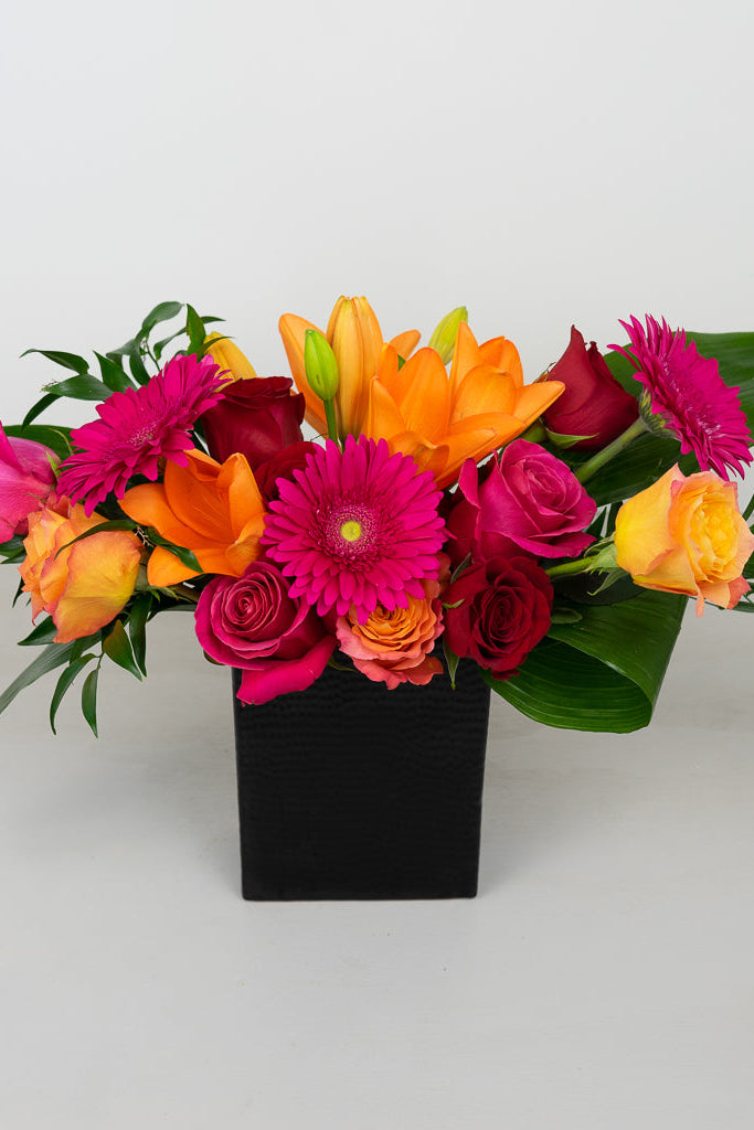 orange lilies, hot pink gerbera daisies, red roses, orange roses in black vase