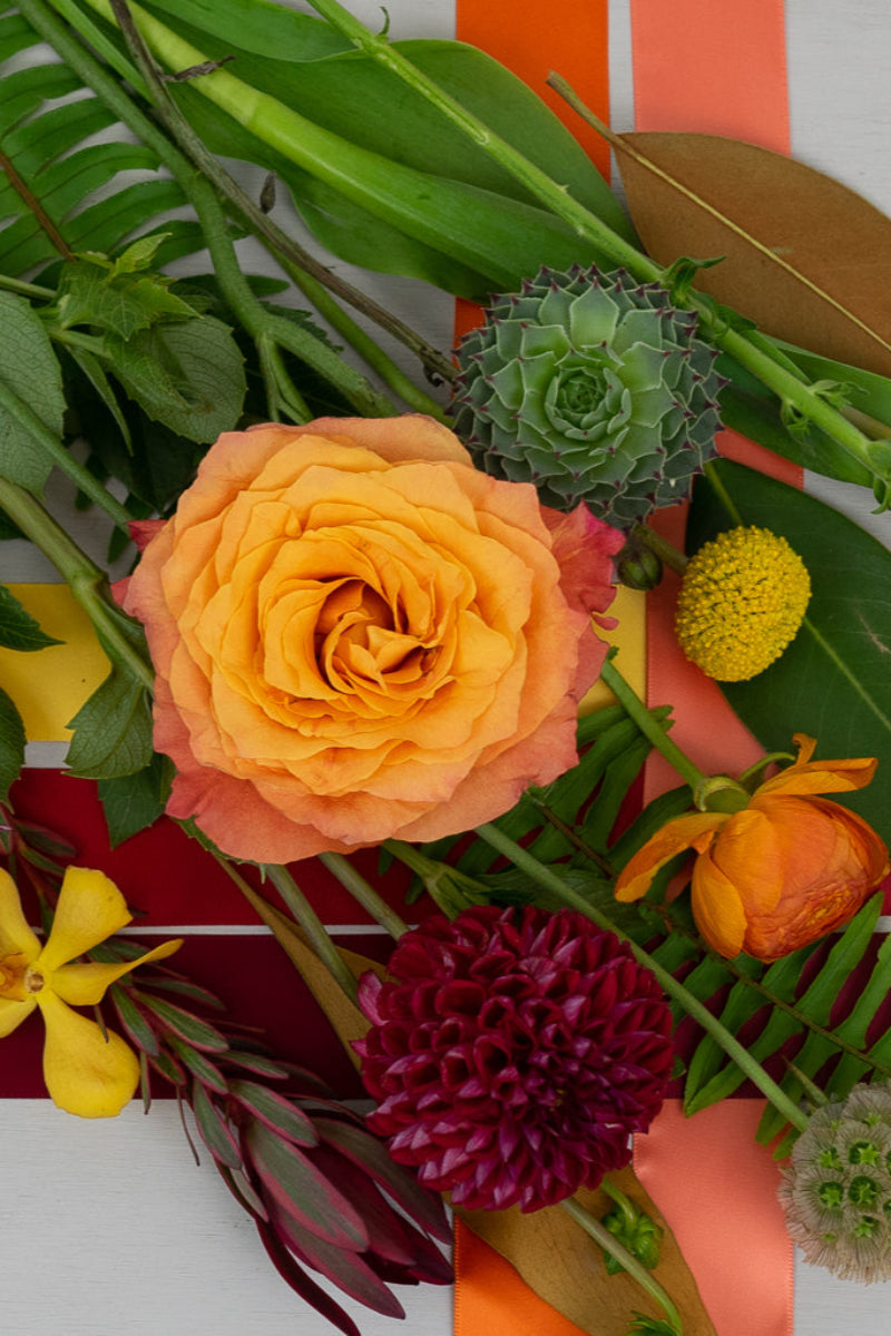 An arrangement of various flowers and foliages in shades of yellow, orange, red, and green.