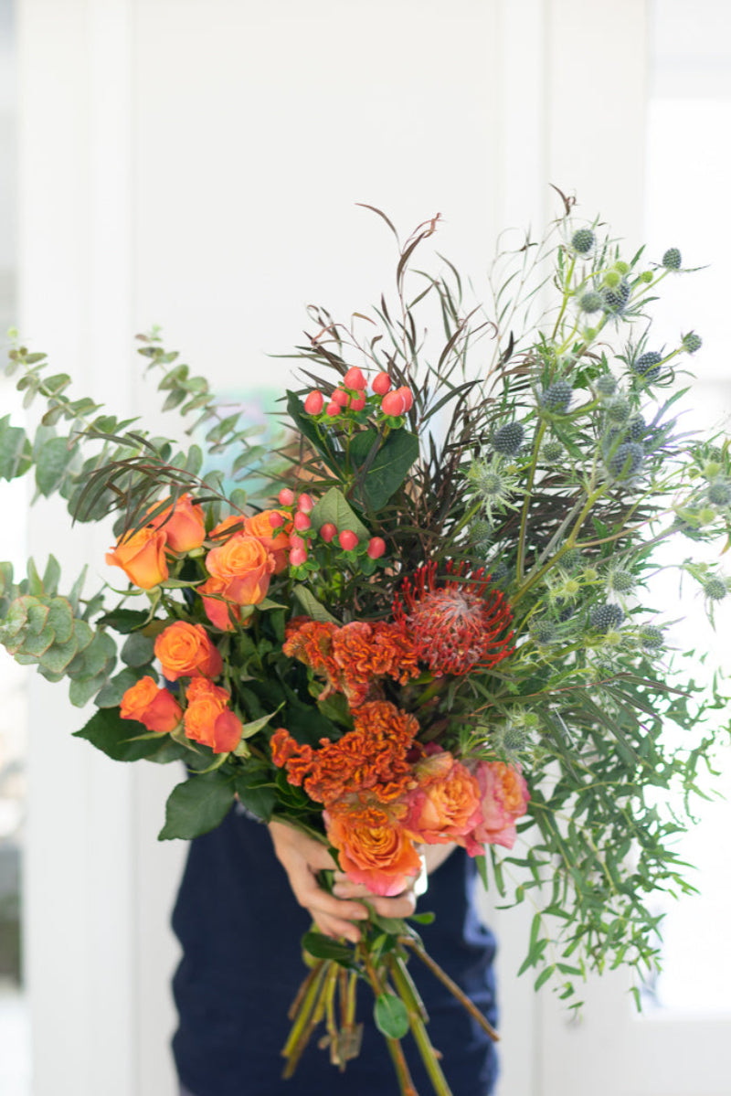 A bunch of colorful flowers including orange, pink, and green, arranged with green foliage and delivered without a vase.