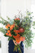 A bunch of colorful flowers including orange, pink, and green, arranged with green foliage and delivered without a vase.