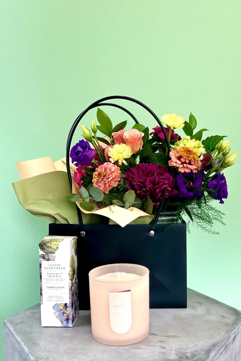 Glow &amp; Bloom gift bundle with cheerful bouquet, candle, and hand cream in black handled gift bag