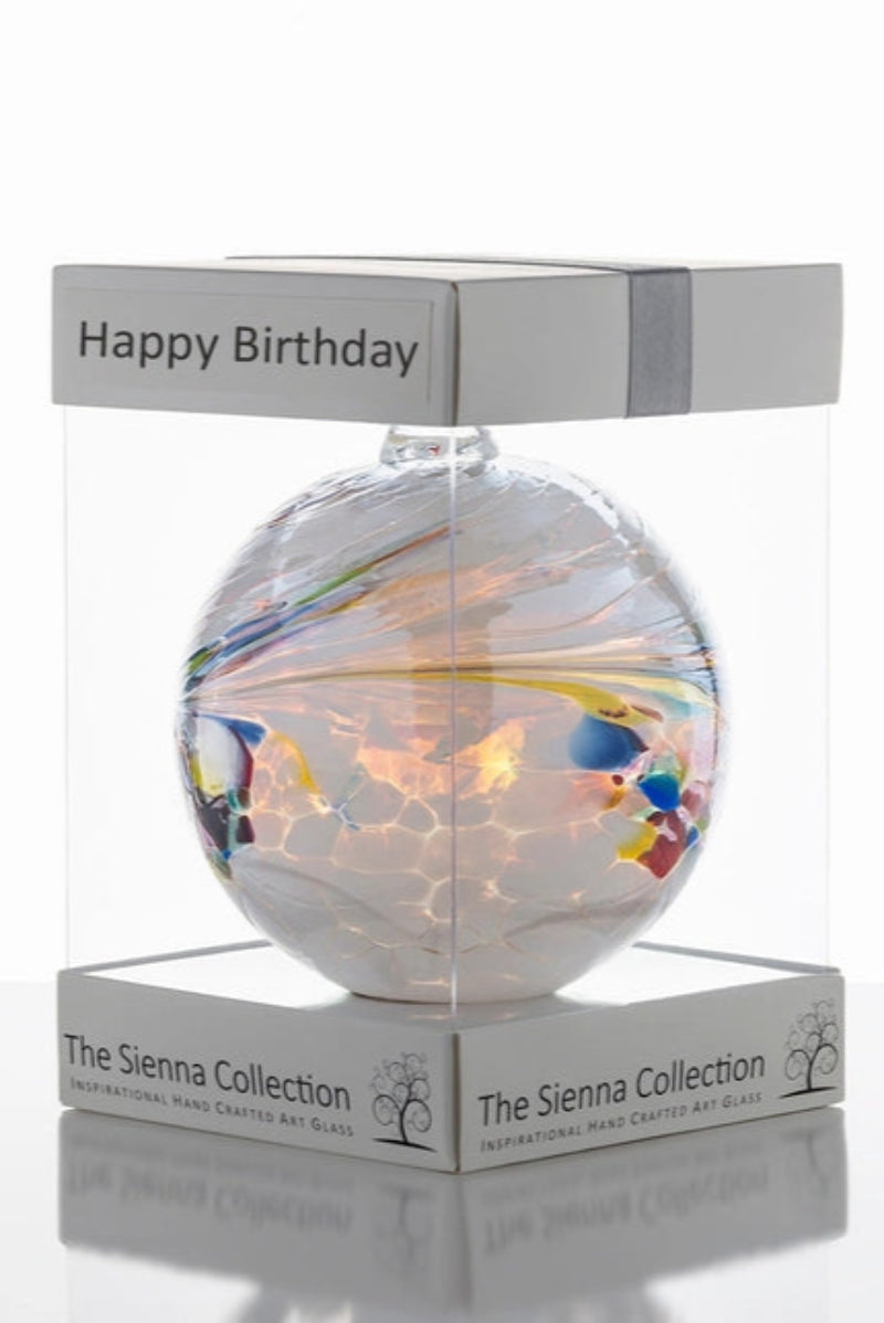 A multicolored glass friendship orb with 'Happy Birthday' text on the packaging, placed inside a clear Sienna gift box.
