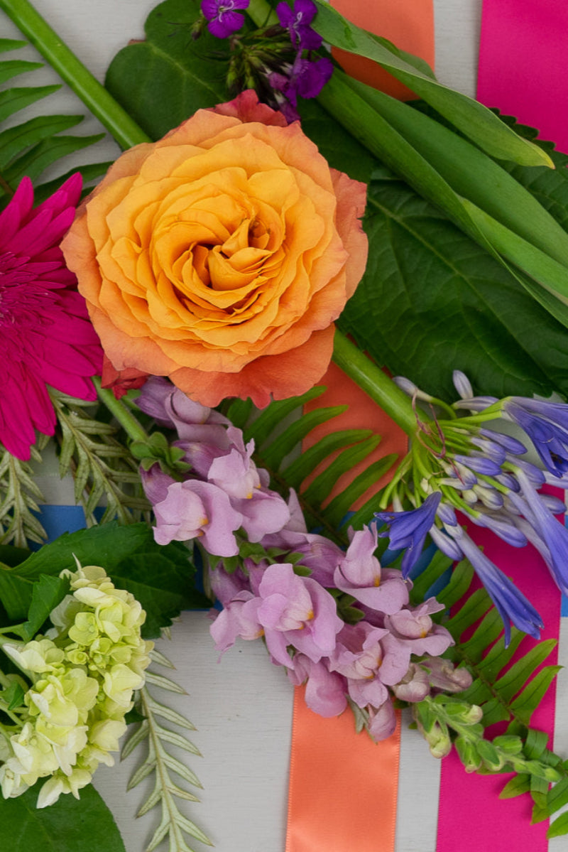 A bouquet of various flowers including pink, purple, orange, and yellow, arranged with green foliage and a decorative ribbon.