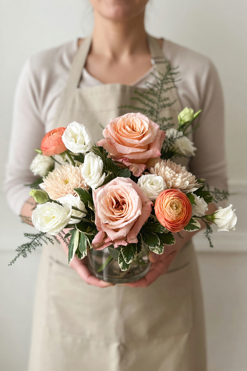 woman holding a pink and white flower arrangement with roses, lisianthus, ranunculus and roses