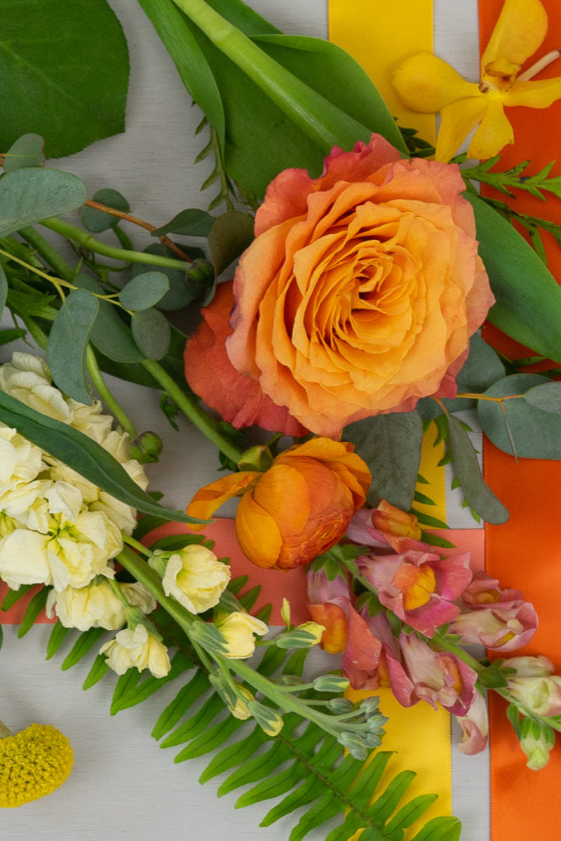 A bouquet of various flowers including yellows, oranges, and greens, arranged to complement a sunny-themed decor.