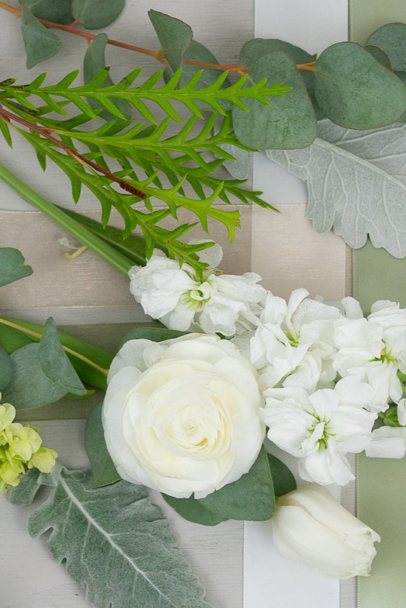 A bouquet of white flowers including roses and green leaves arranged on a neutral background.