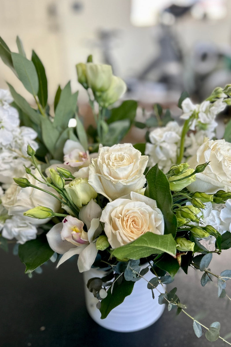 Bouquet of white flowers with green leaves in a vase on a blurred background