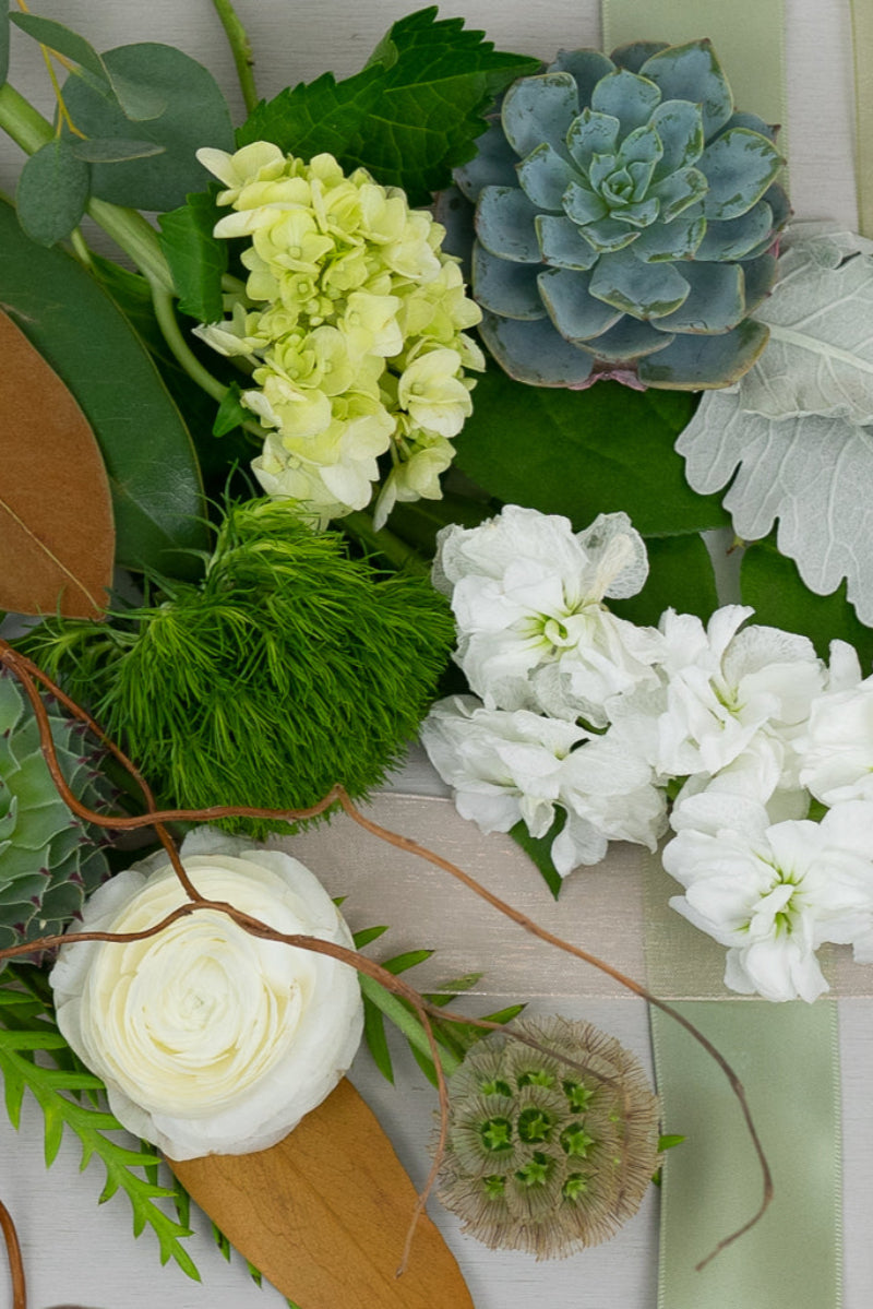 A bouquet of various flowers including white and green foliage, arranged in a seasonal arrangement on a wooden surface.