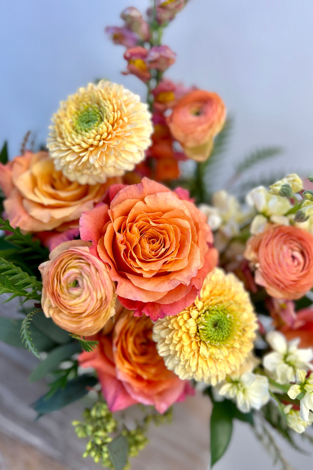 Close‑up of the Apricot Honey bouquet featuring soft yellow stock, coral roses, snapdragons, and ranunculus with mixed green foliage, highlighting fresh premium blooms and modern floral design.