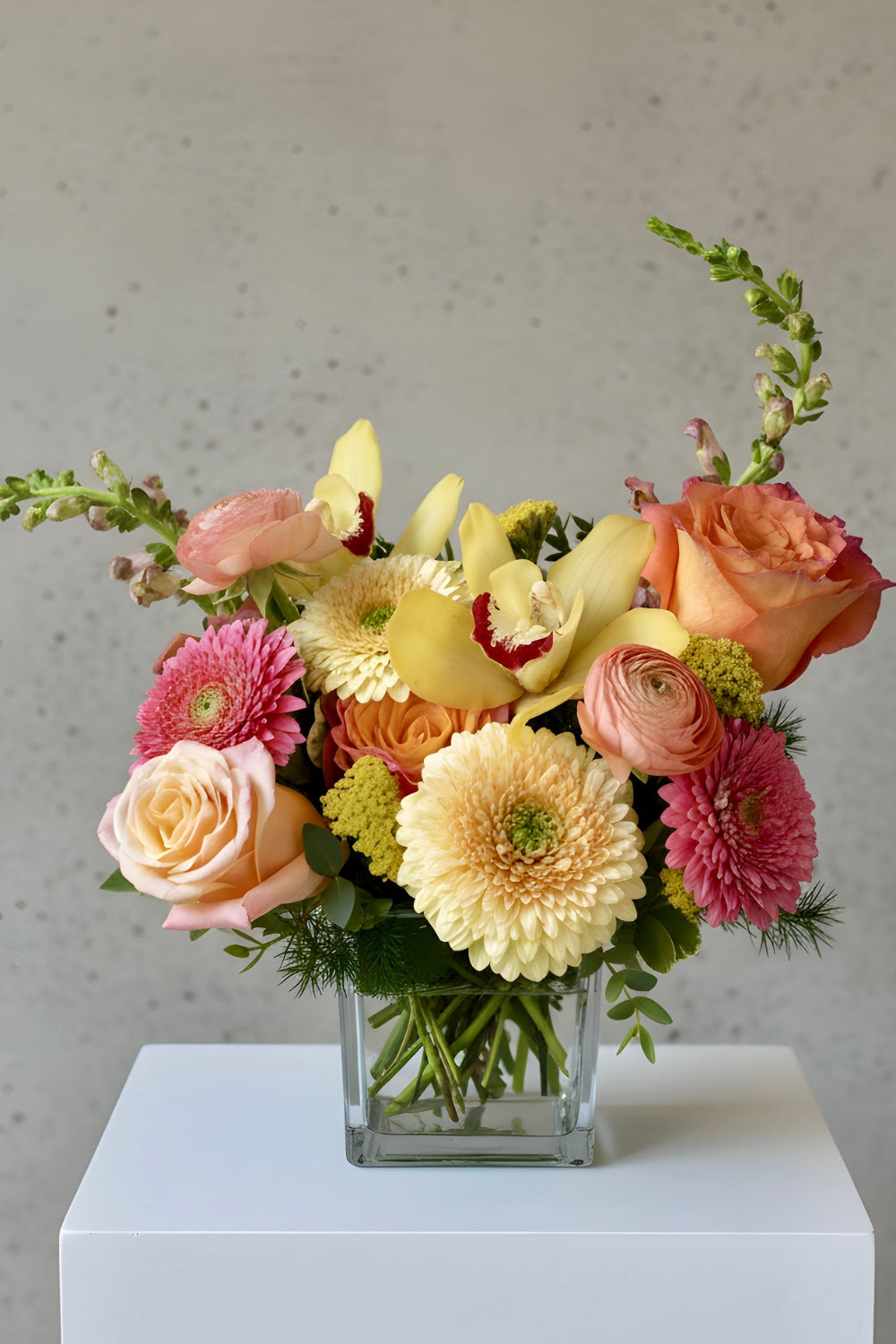 Sunny peach, pink and yellow bouquet with roses, gerbera daisies, orchids designed in a vase.