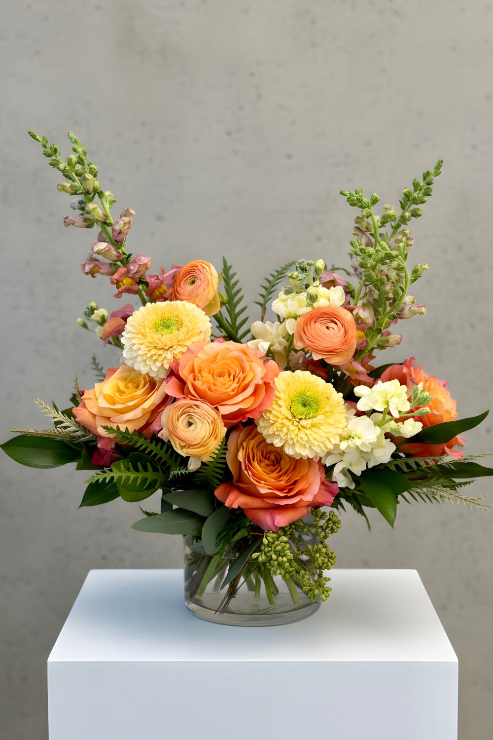 Apricot Honey bouquet with soft yellow stock, coral roses, snapdragons, and ranunculus arranged with mixed green foliage in a modern floral design.