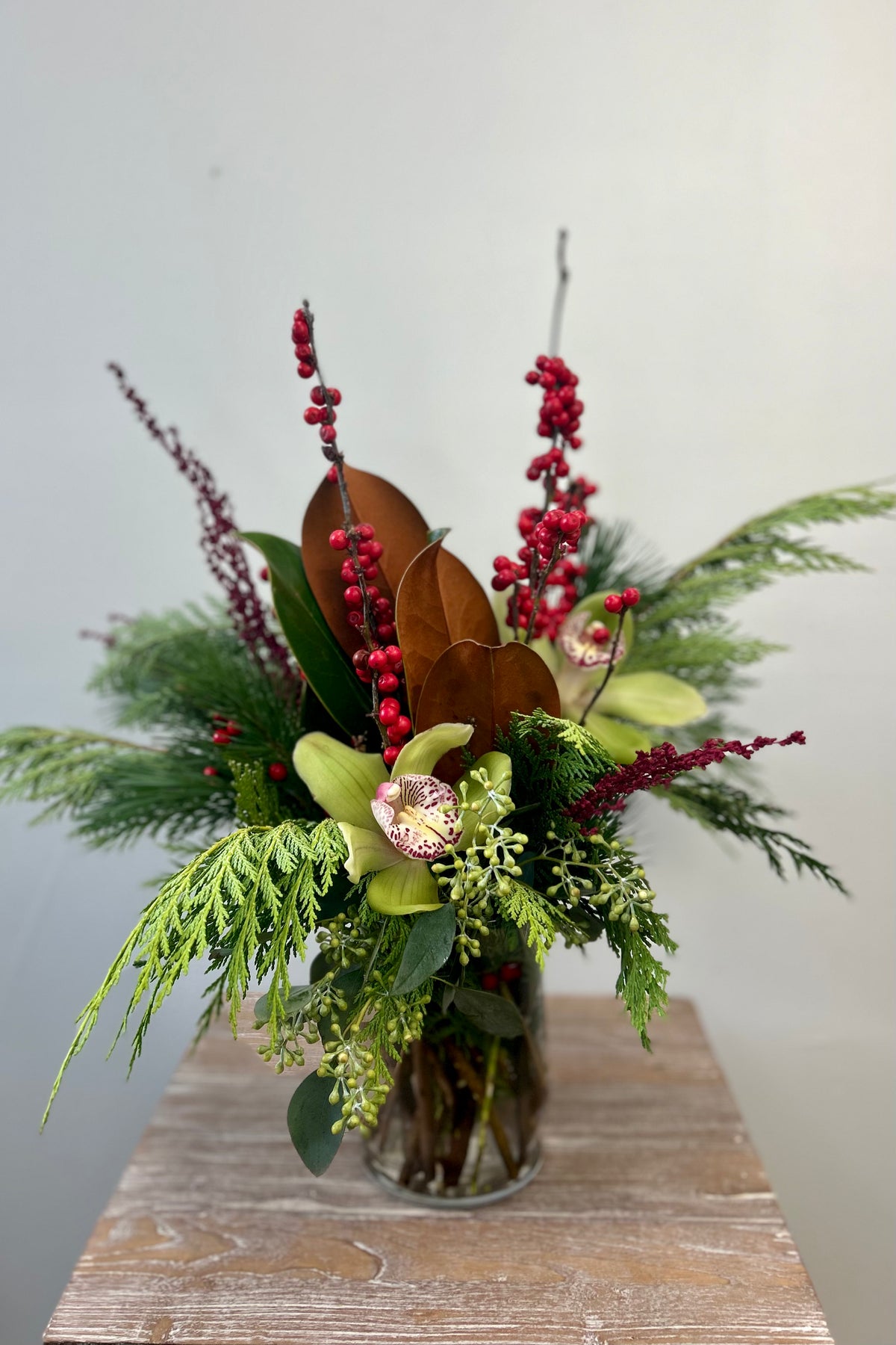 Berry Bright Blooms holiday bouquet with evergreens, red ilex berries, and green cymbidium orchids