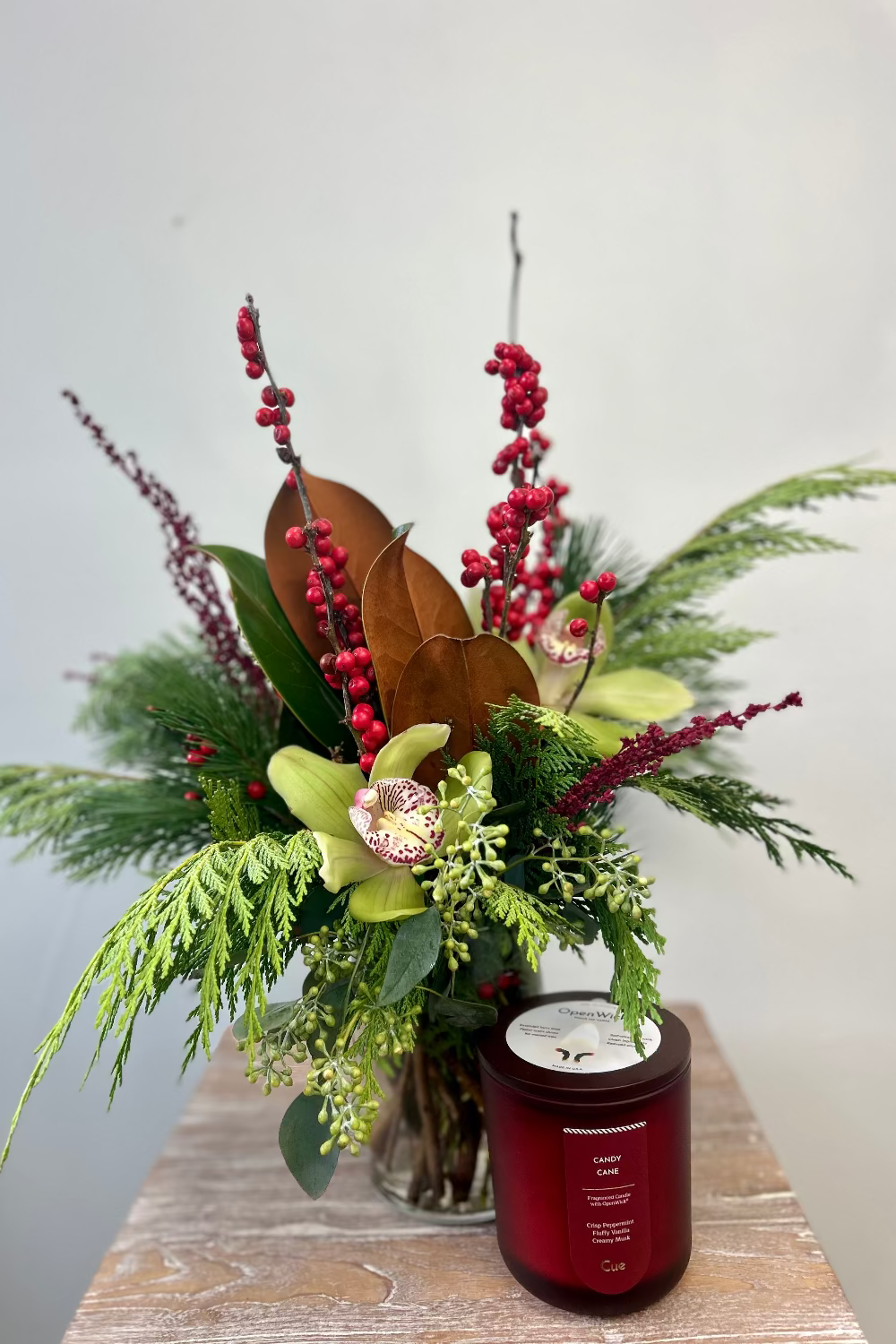 Berry Bright Blooms bouquet displayed in festive holiday setting with evergreens, orchids, and berries