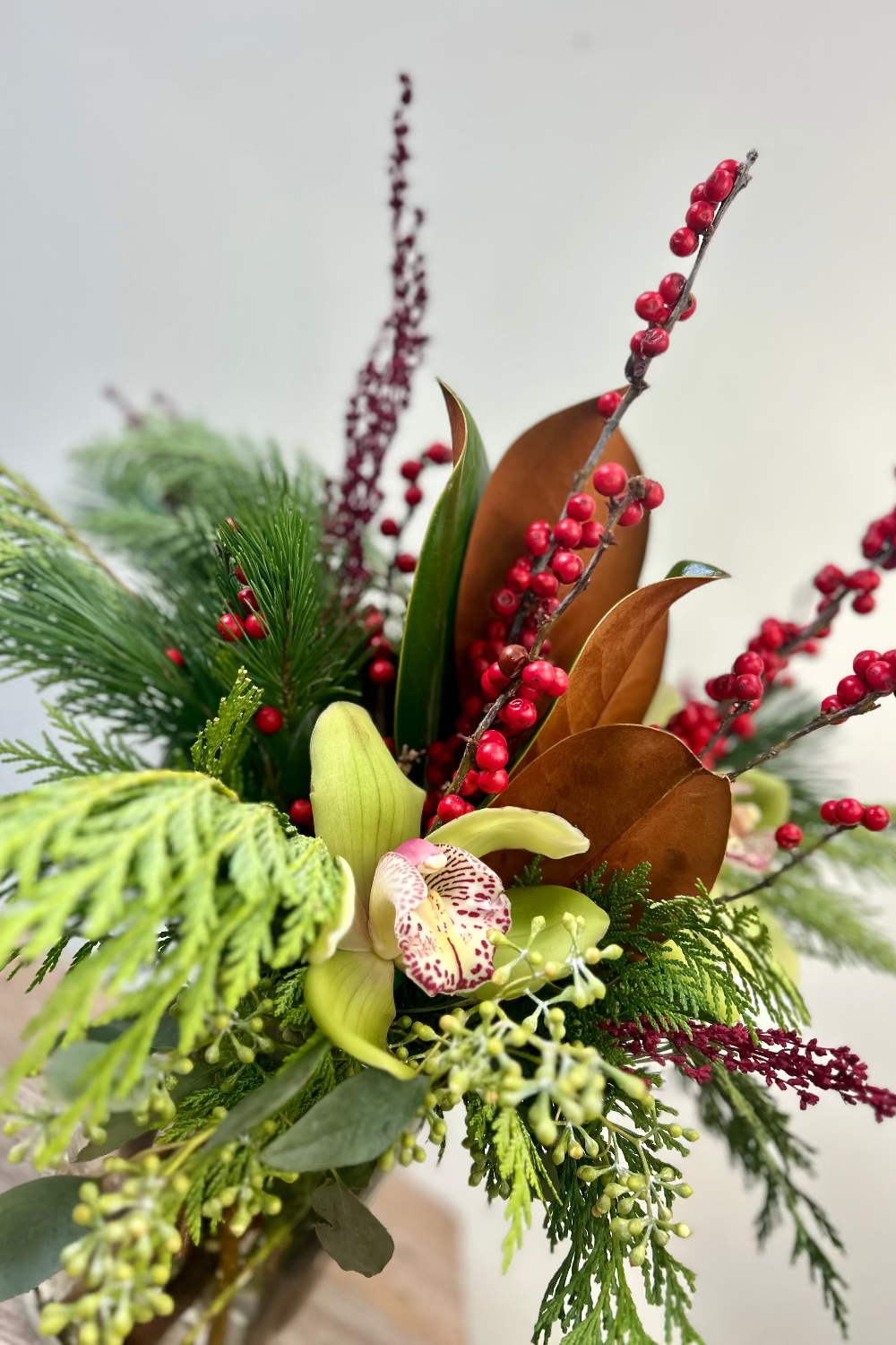 Close‑up of Berry Bright Blooms bouquet showing green cymbidium orchids with red ilex berries