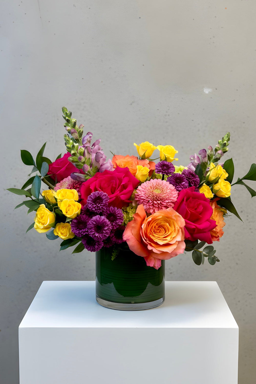 Colorful flower arrangement in a vase on a white pedestal against a gray background