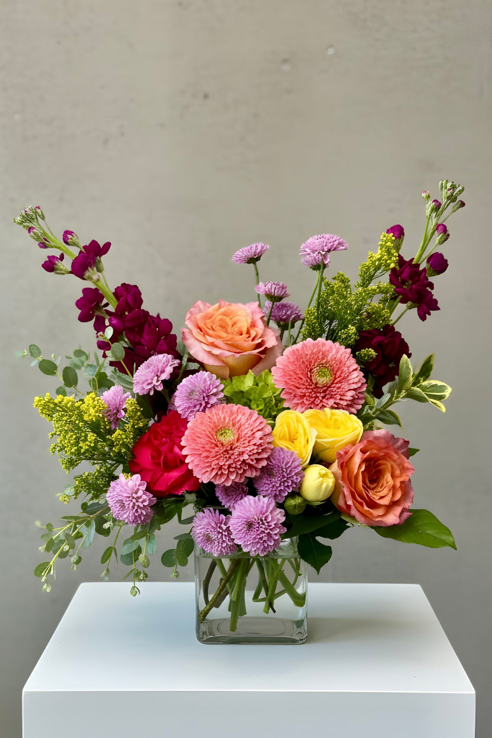 Bloomfetti Petite bouquet in bright spring colors arranged in a clear vase, styled simply on a white surface