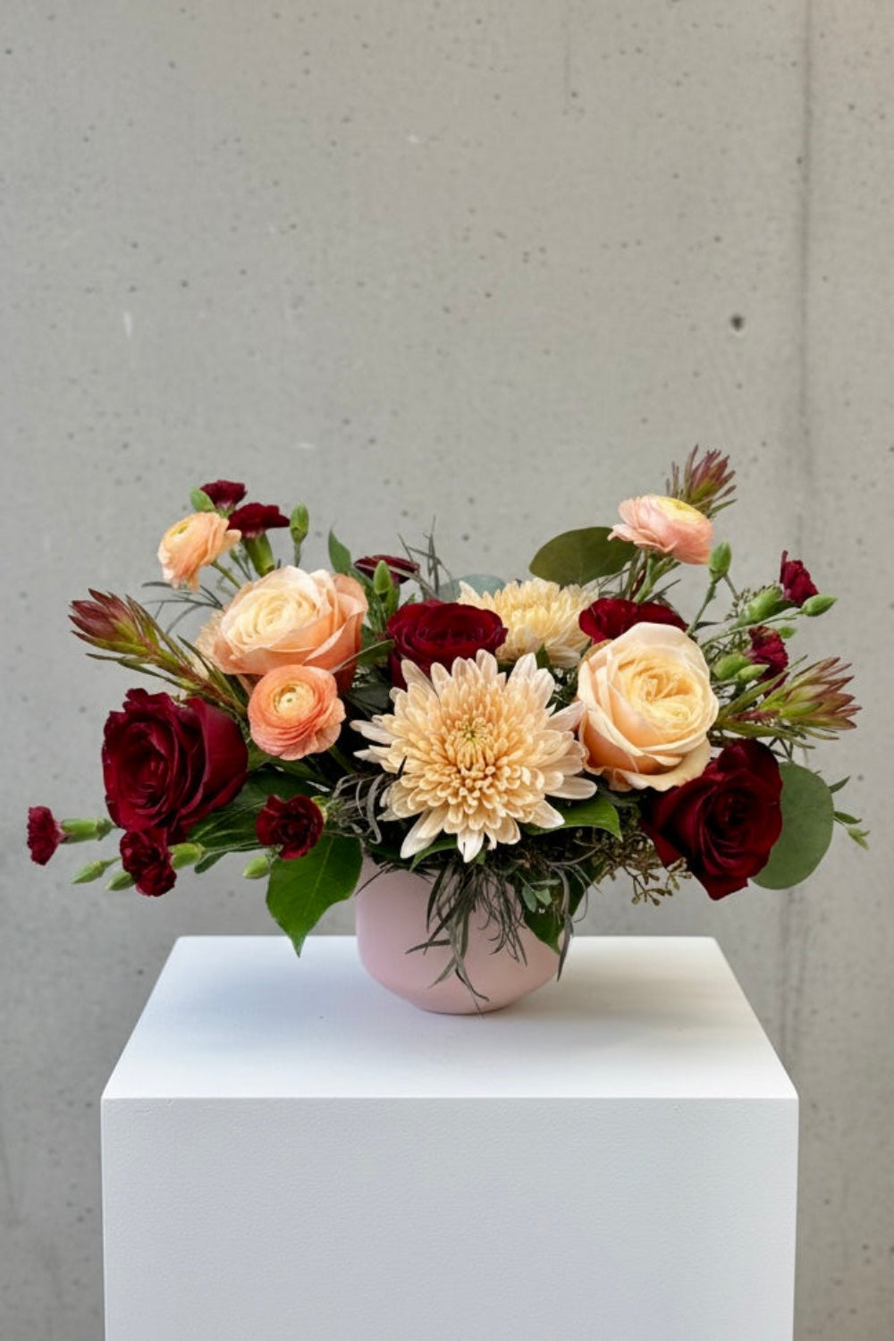 Blush &amp; Bordeaux Bloom Vase with burgundy roses, blush roses, café latte cremones, peach ranunculus, safari sunset, and eucalyptus arranged in a blush vase standard size
