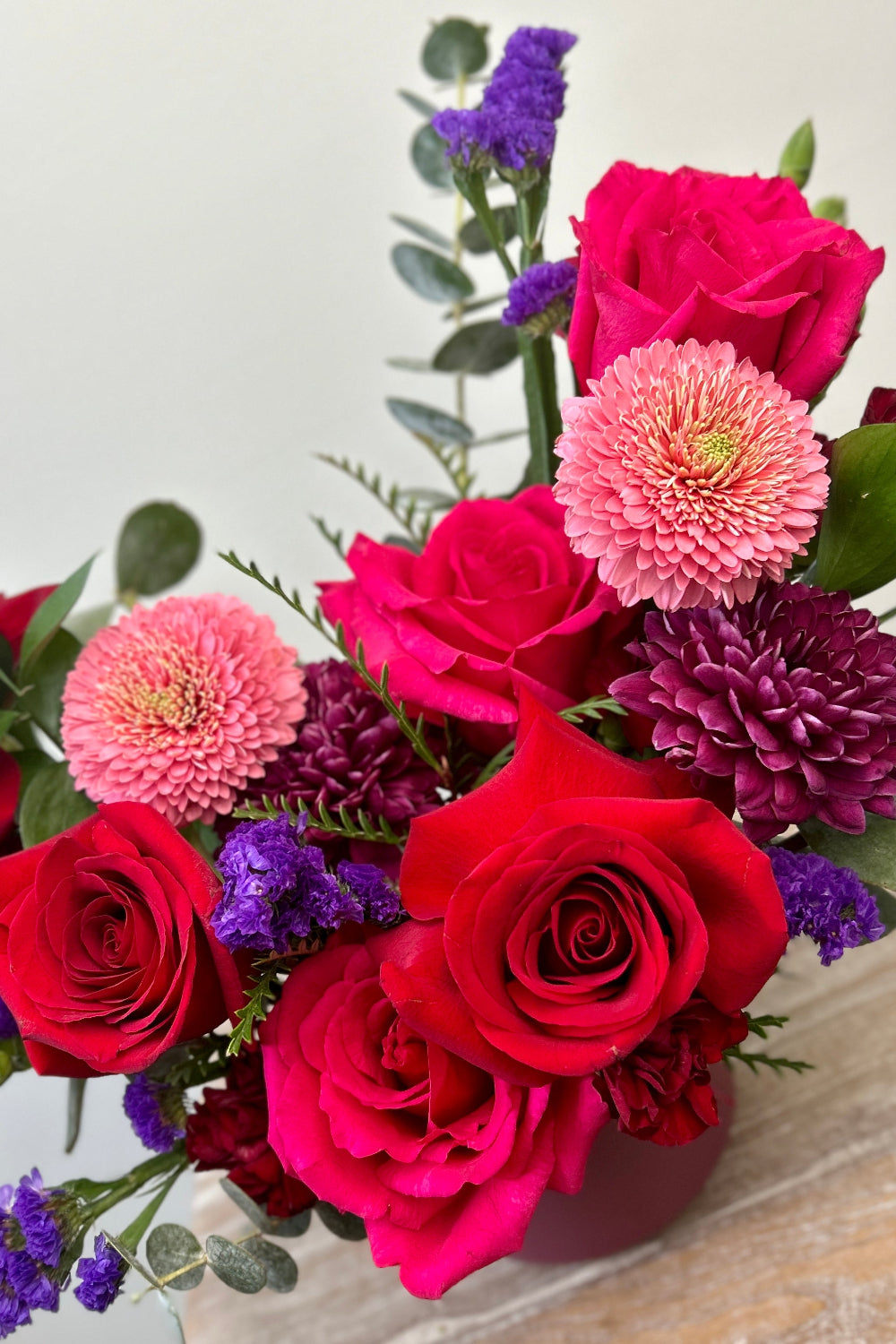 Close-up of Valentine Color Crush showing red roses, hot pink roses, purple cremones, pink germinis, statice, and pixie carnations.