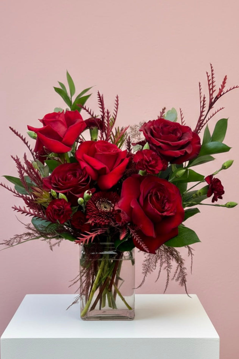 Crimson Obsession bouquet with Black Pearl roses, red Freedom roses, red cremones, burgundy pixie carnations, and red foliage arranged in a rectangular glass vase.