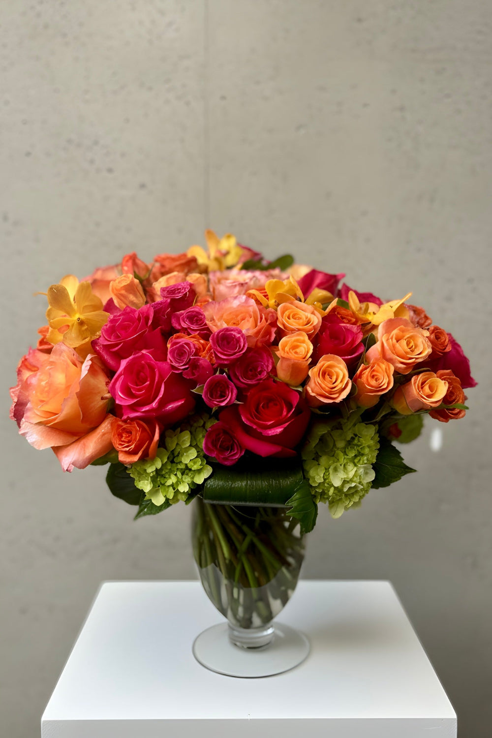 Bouquet of colorful roses in a clean geometric shape in a glass vase with modern foliage