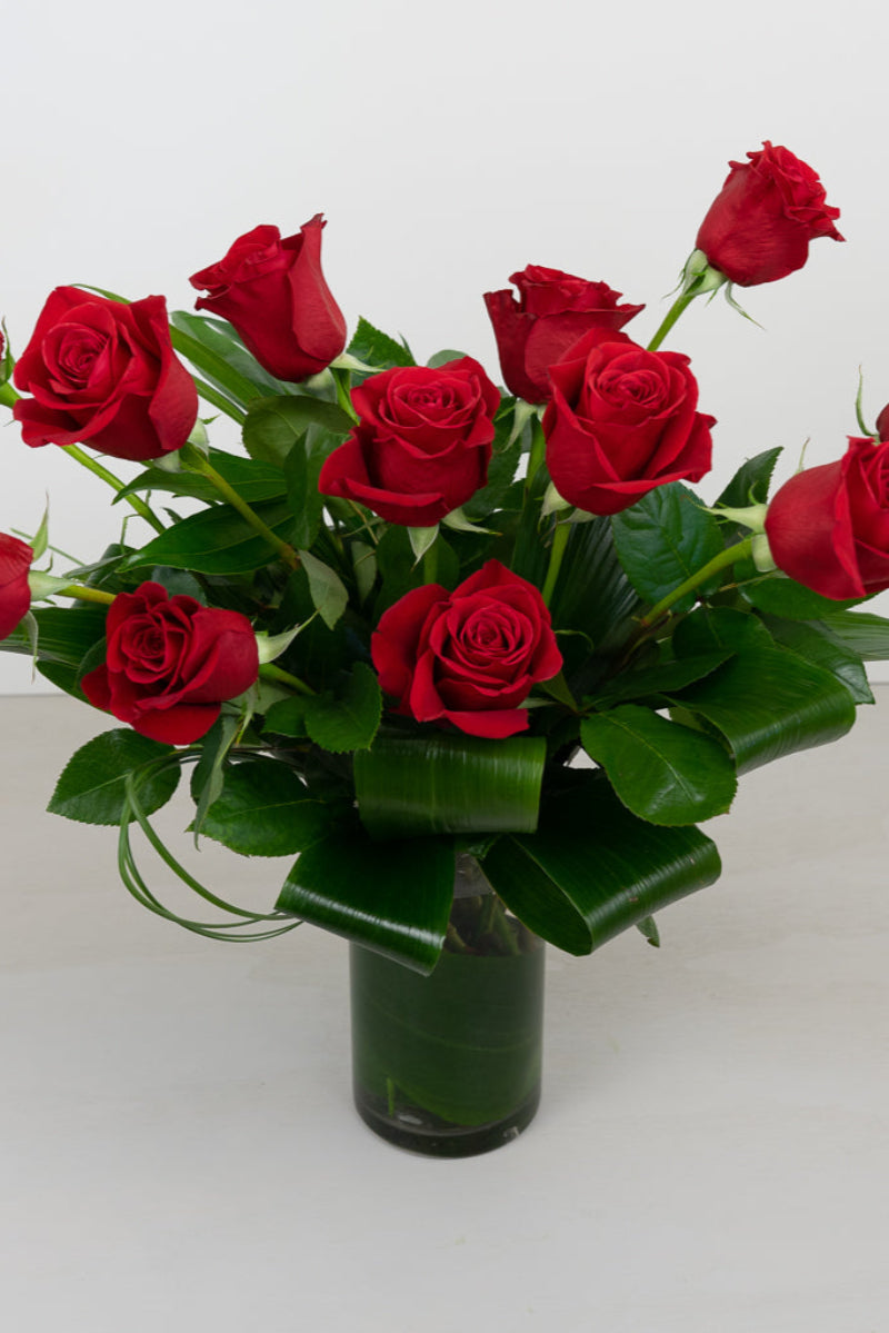 A bouquet of red roses arranged in a clear glass vase with green foliage.
