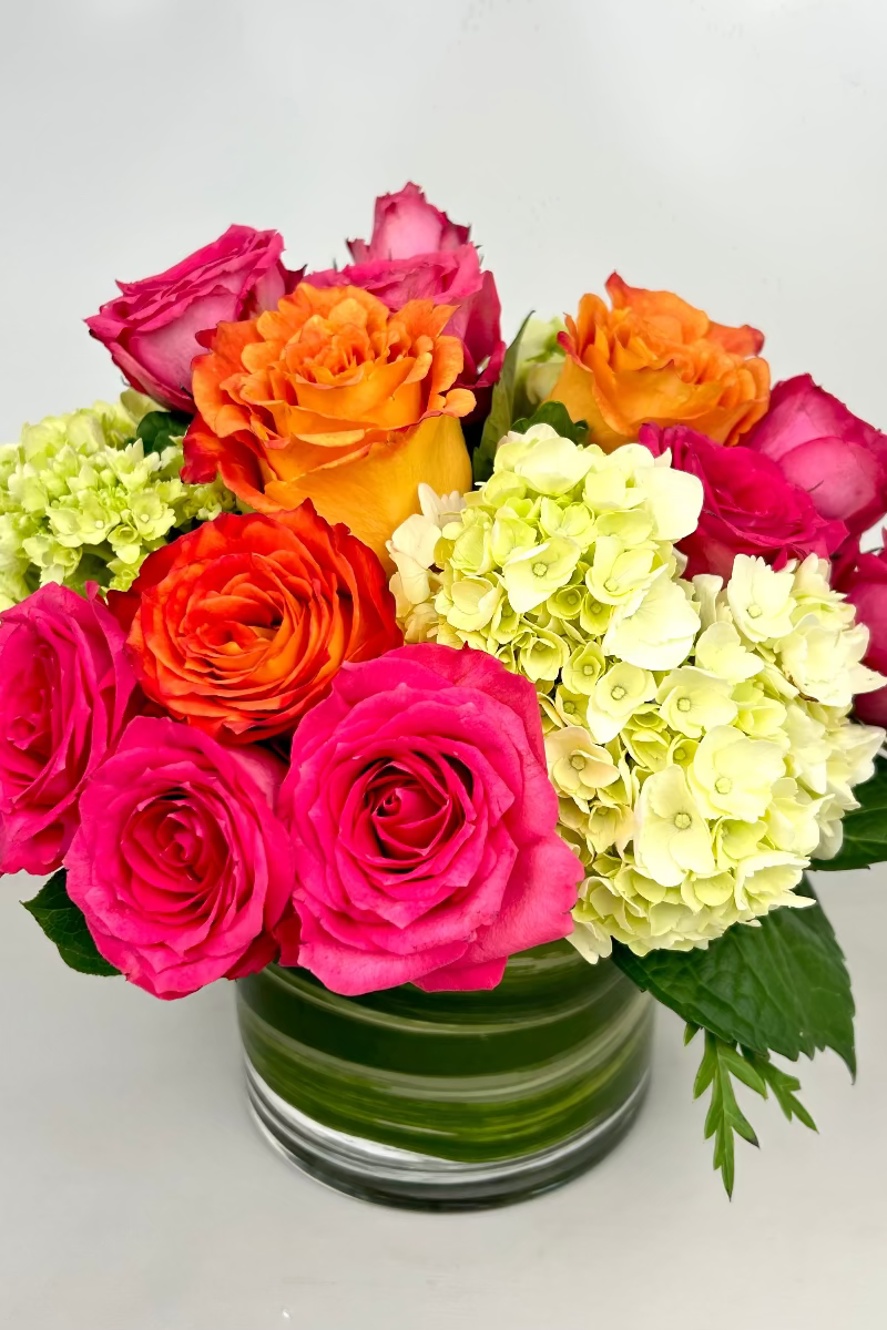 A colorful bouquet of pink, orange, and green flowers in a clear glass vase, representing the &#39;Fruit Punch Bouquet&#39; with roses, spray roses, and hydrangea.