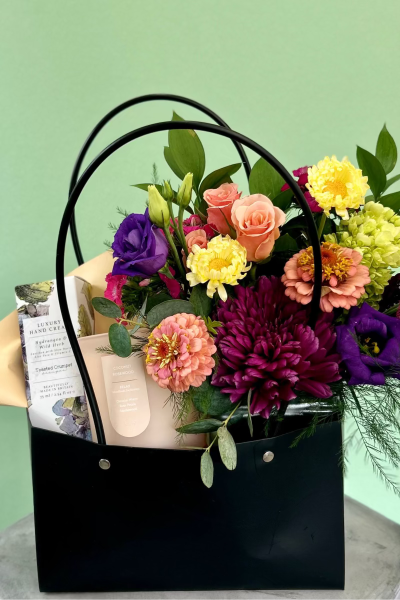 Glow &amp; Bloom gift bundle with cheerful bouquet, candle, and hand cream in black handled gift bag close up