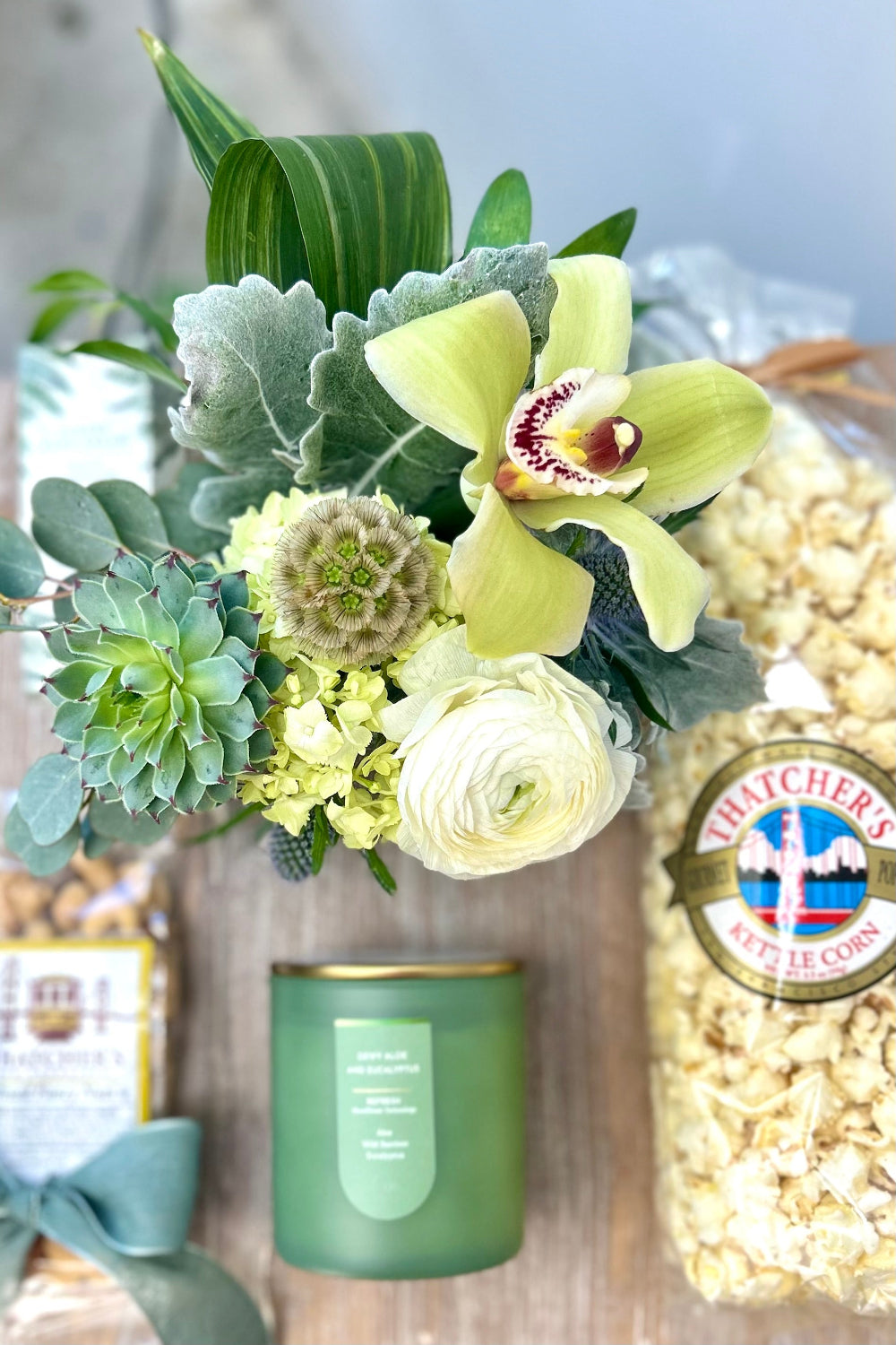 Bouquet of soft cream and green flowers with a candle and a bag of popcorn mixed nuts hand cream packaged for a luxury gift for delivery