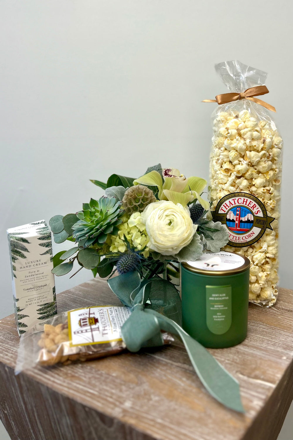 soft green and cream flower  arrangement with succulents and orchids, a &quot;refresh&quot; green and gold candle, kettle cooked popcorn, mixed nuts with a green bow, hand cream as a luxury gift set for delivery in Lone Tree Colorado