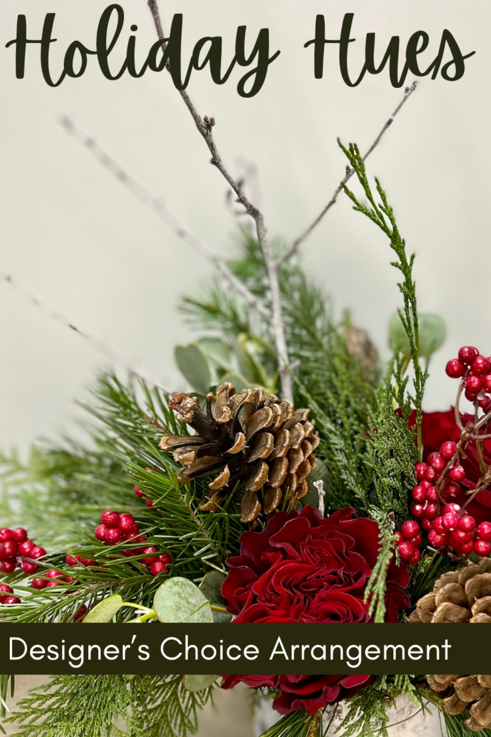 Holiday-themed floral arrangement with greenery, red flowers, and pinecones on a neutral background.