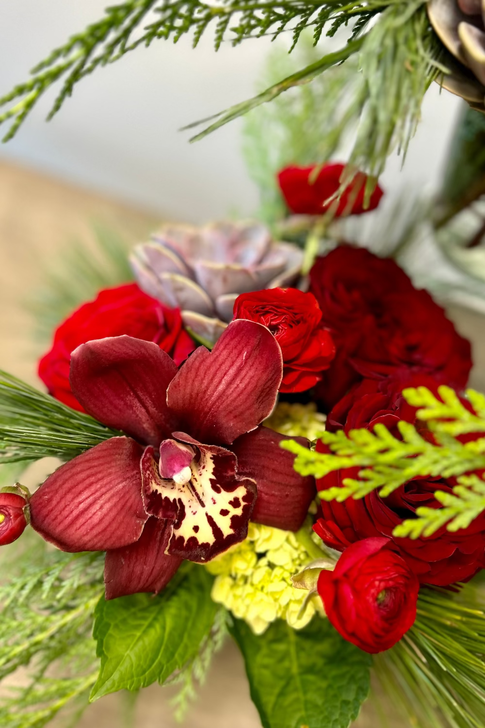 red bouquet with evergreens orchids ranunculus roses and succulents