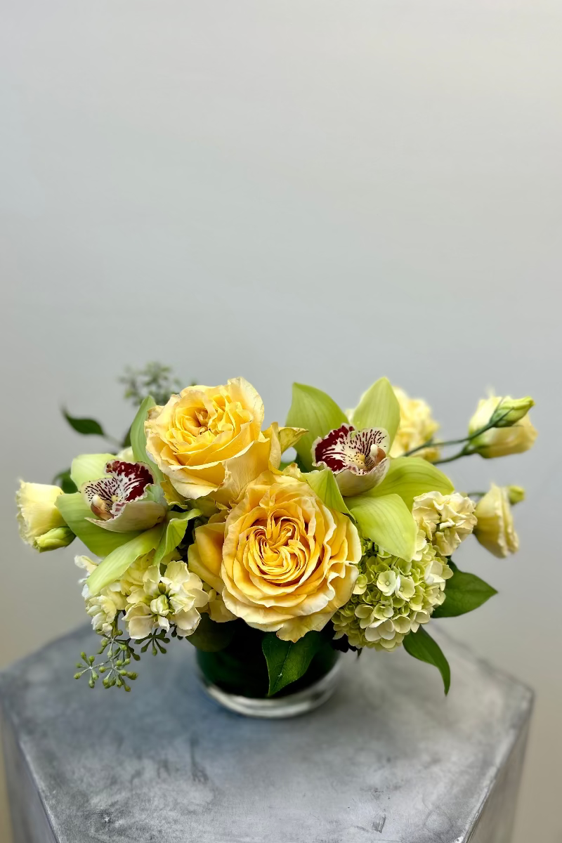 Petite Lemon &amp; Light bouquet on a bedside table featuring soft yellow lisianthus, green hydrangeas, and eucalyptus in a glass vase