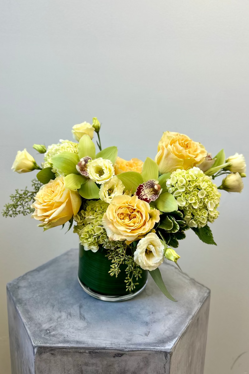 Signature style Lemon & Light bouquet with soft yellow lisianthus, garden roses, green hydrangeas, cymbidiums, and eucalyptus in a glass cylinder