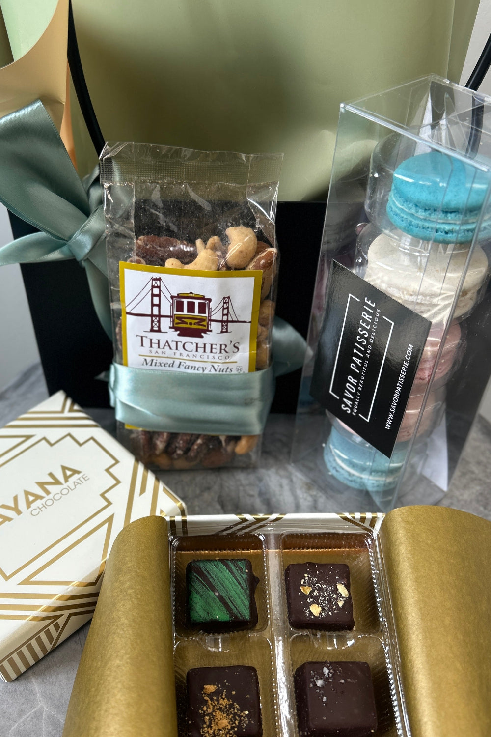 A Father’s Day gift set featuring a small succulent, artisan chocolates, unicorn macarons, and premium mixed nuts arranged in a premium gift bag close up of food items