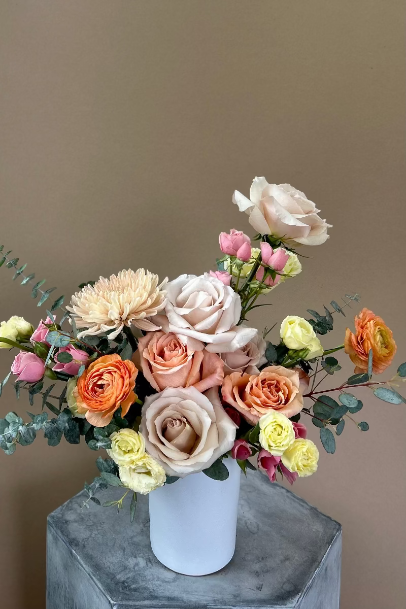 Pale Drift signature bouquet with muted peach, butter yellow, pale pink, and blush blooms in a matte white vase