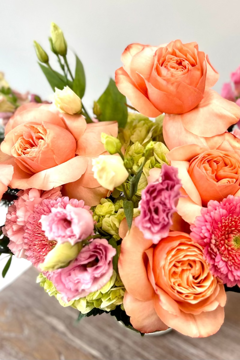 Bouquet of pink and peach flowers on a wooden surface with a light background