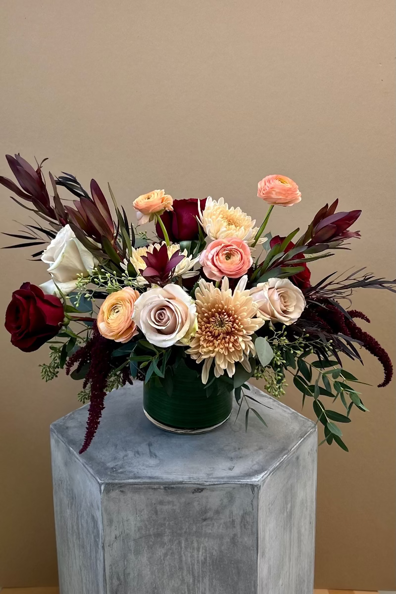 Rosé Ember signature bouquet with burgundy safari sunset, blush roses, peach ranunculus, cremones, and eucalyptus in a loose, airy design