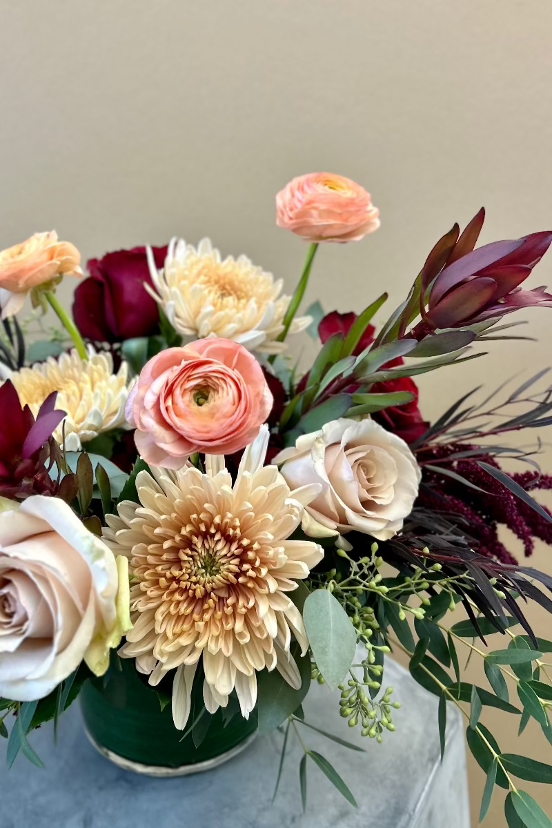 Close-up of Rosé Ember bouquet showing layered blush and peach roses, burgundy accents, and trailing amaranthus