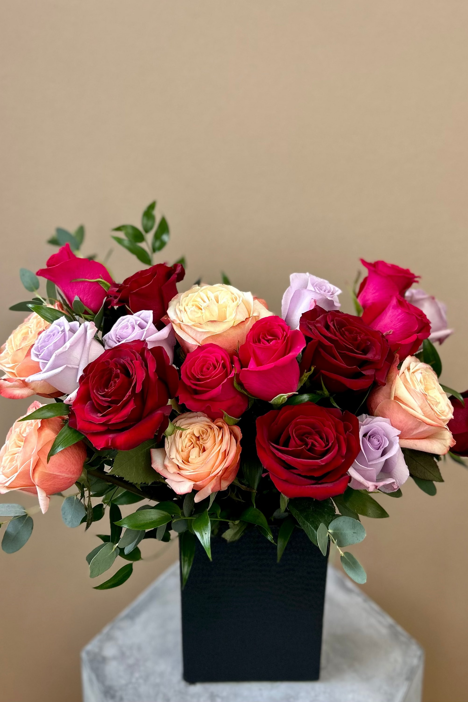 Rosé Riche premium bouquet with deep crimson, hot pink, light pink, and lavender roses in a matte black vase