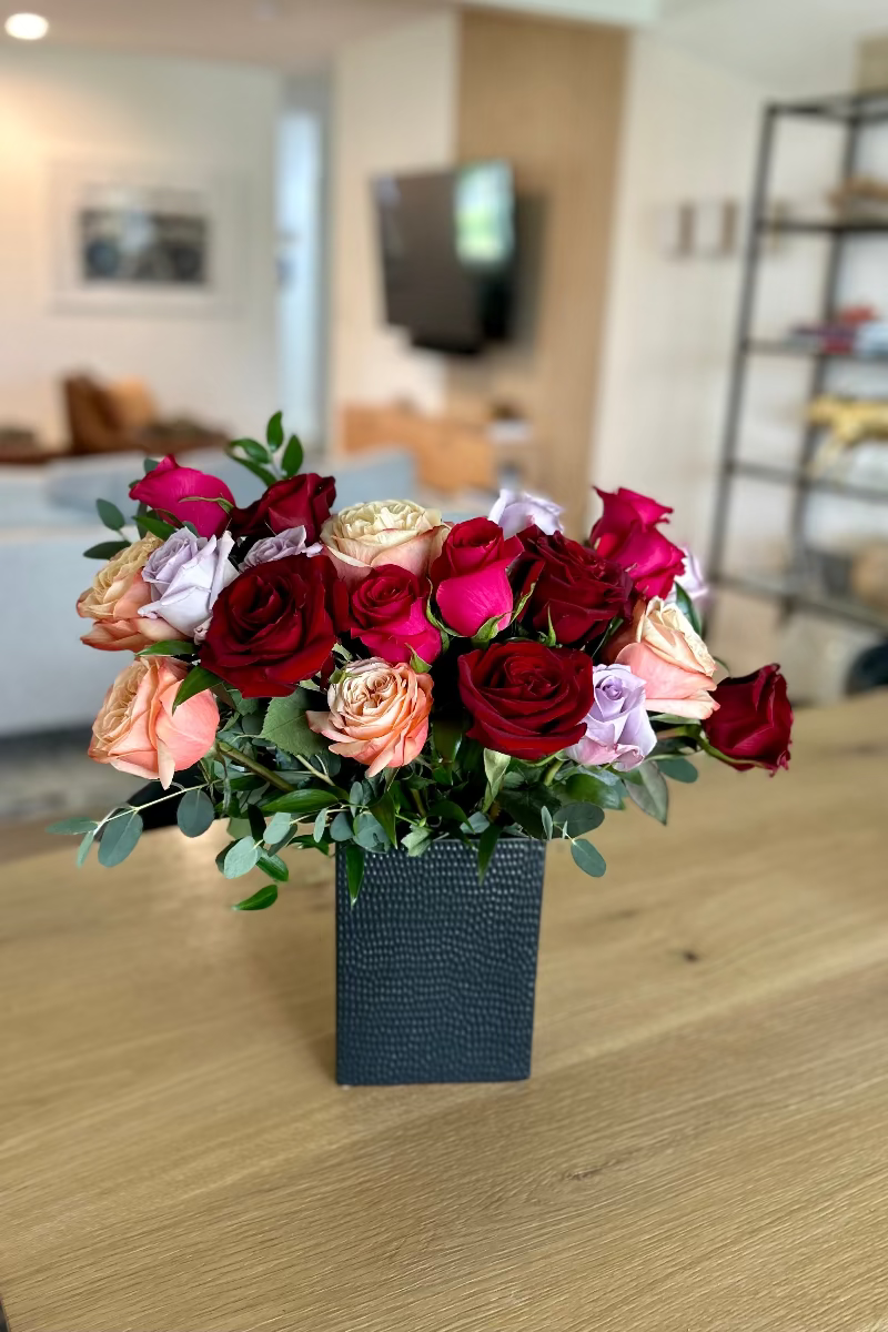 Rosé Riche standard bouquet with 16 stems of crimson, hot pink, light pink, and lavender roses in a black vase