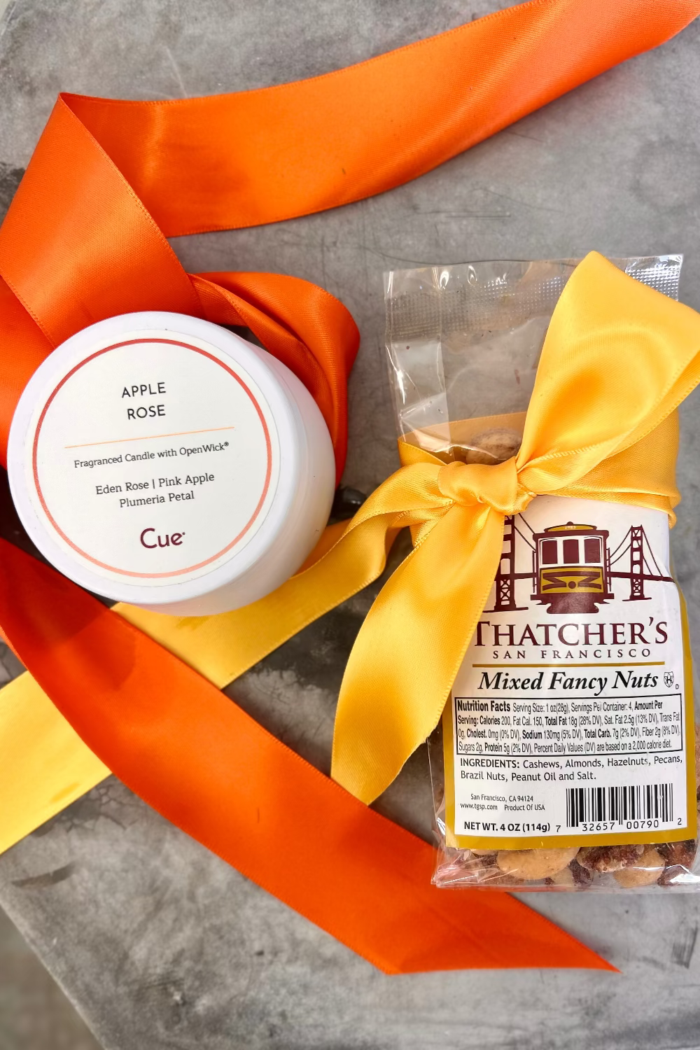 Cue apple rose candle and Thatcher&#39;s mixed fancy nuts with orange and yellow ribbons on a gray surface