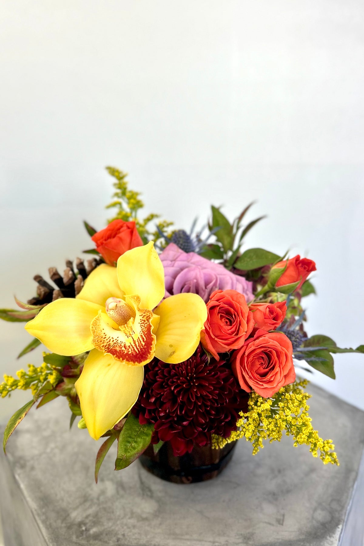 Amber Radiance Trio bouquet in rustic wood barrel with mums, spray roses, orchids, thistles, pinecones, and seasonal foliage