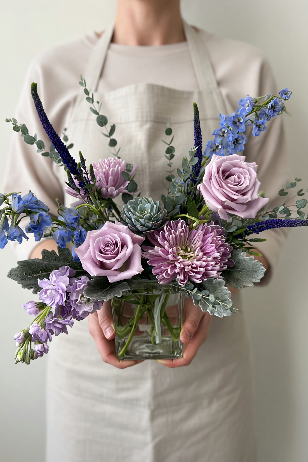 Petite Sanctuary Pastels bouquet with soft lavender, blue, sage green and purple flowers arranged in a garden‑style design being held by local castle pines florist
