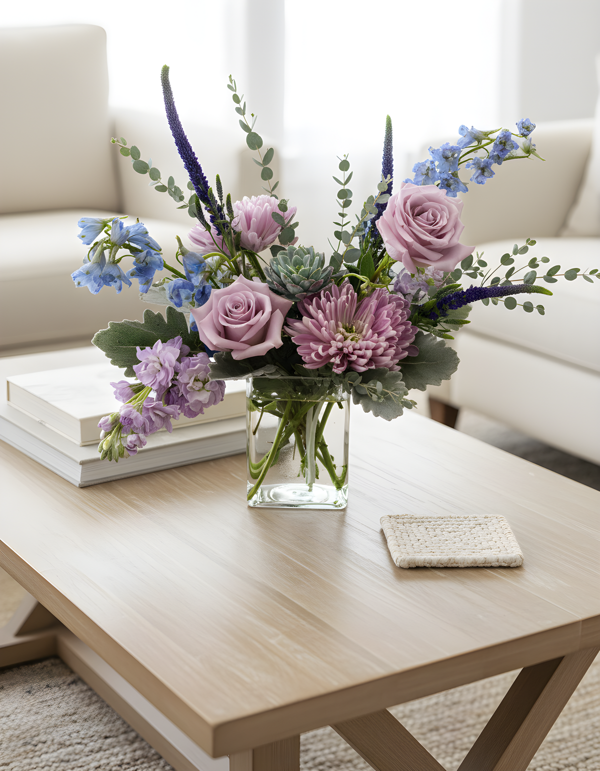 Petite Sanctuary Pastels bouquet with soft lavender, blue, sage green and purple flowers arranged in a garden‑style design on coffee table