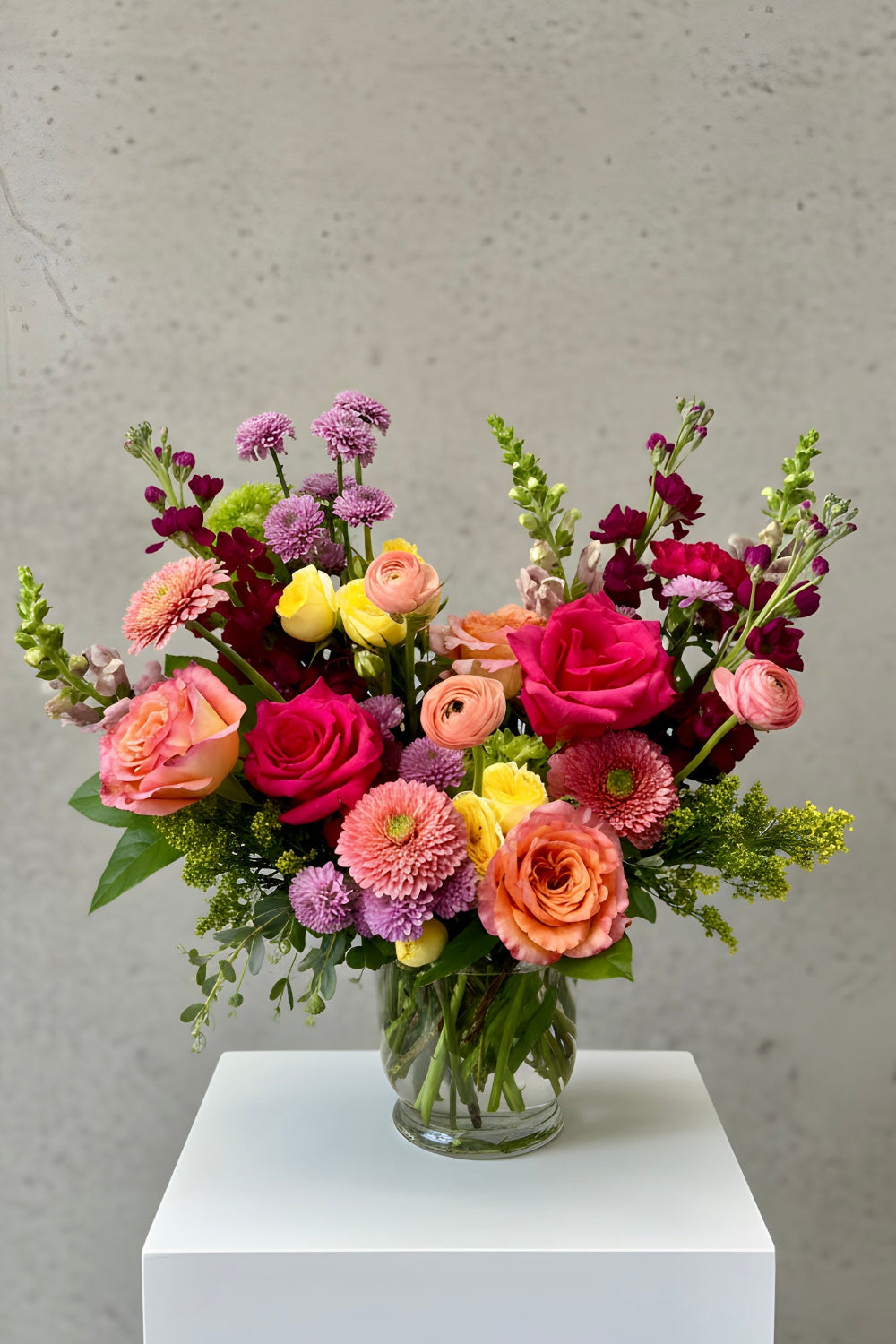 Bloomfetti Petite bouquet in bright spring colors arranged in a clear vase, styled simply on a white surface