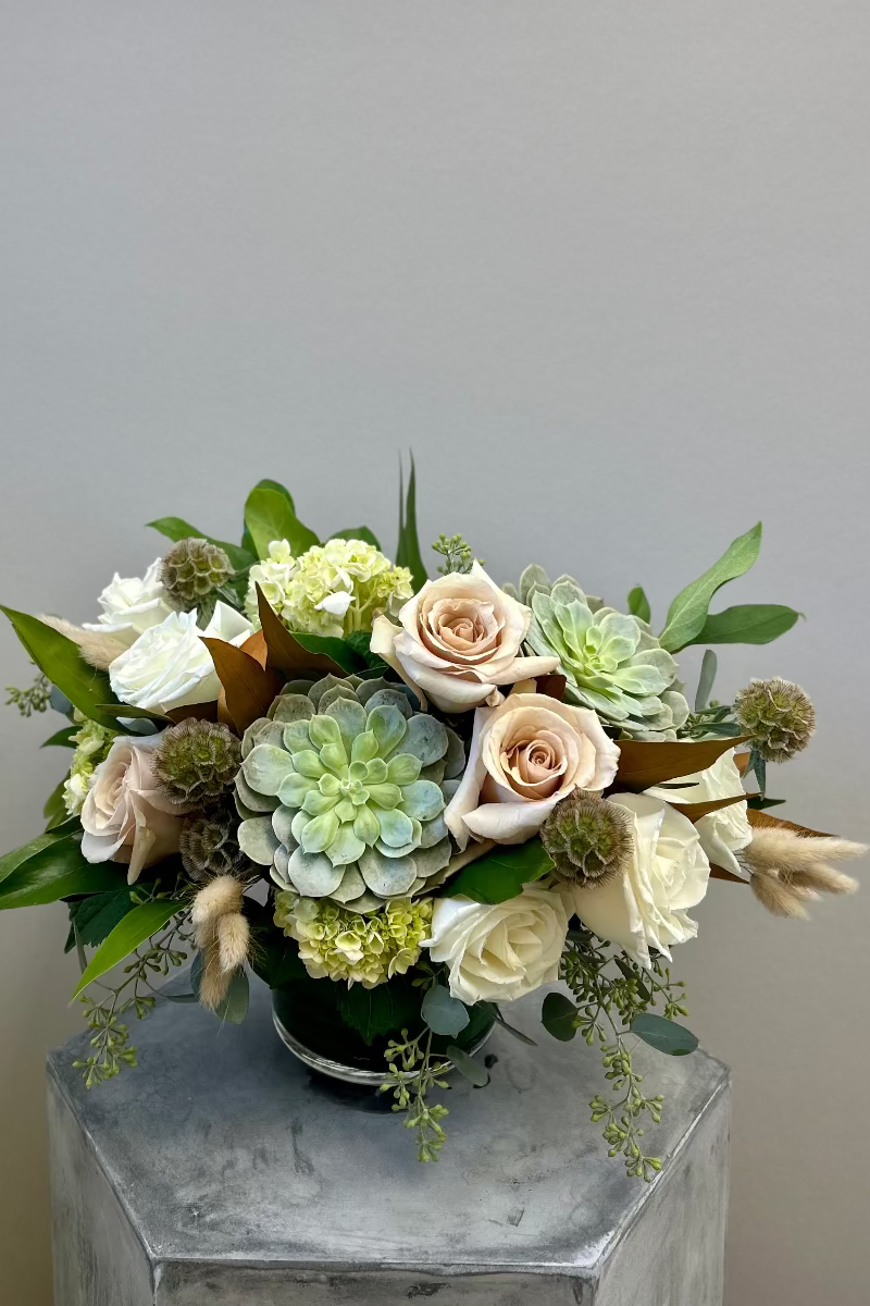 Stillness and Sage bouquet with tan and cream roses, green hydrangeas, succulents, scabiosa pods, and magnolia foliage