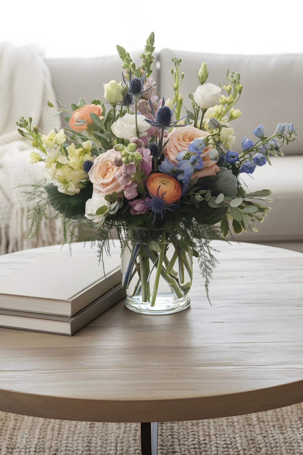 Summer Sorbet pastel summer flower arrangement placed on a coffee table with loose, airy blooms including stock, delphinium, snapdragons, lisianthus, ranunculus, and eucalyptus.