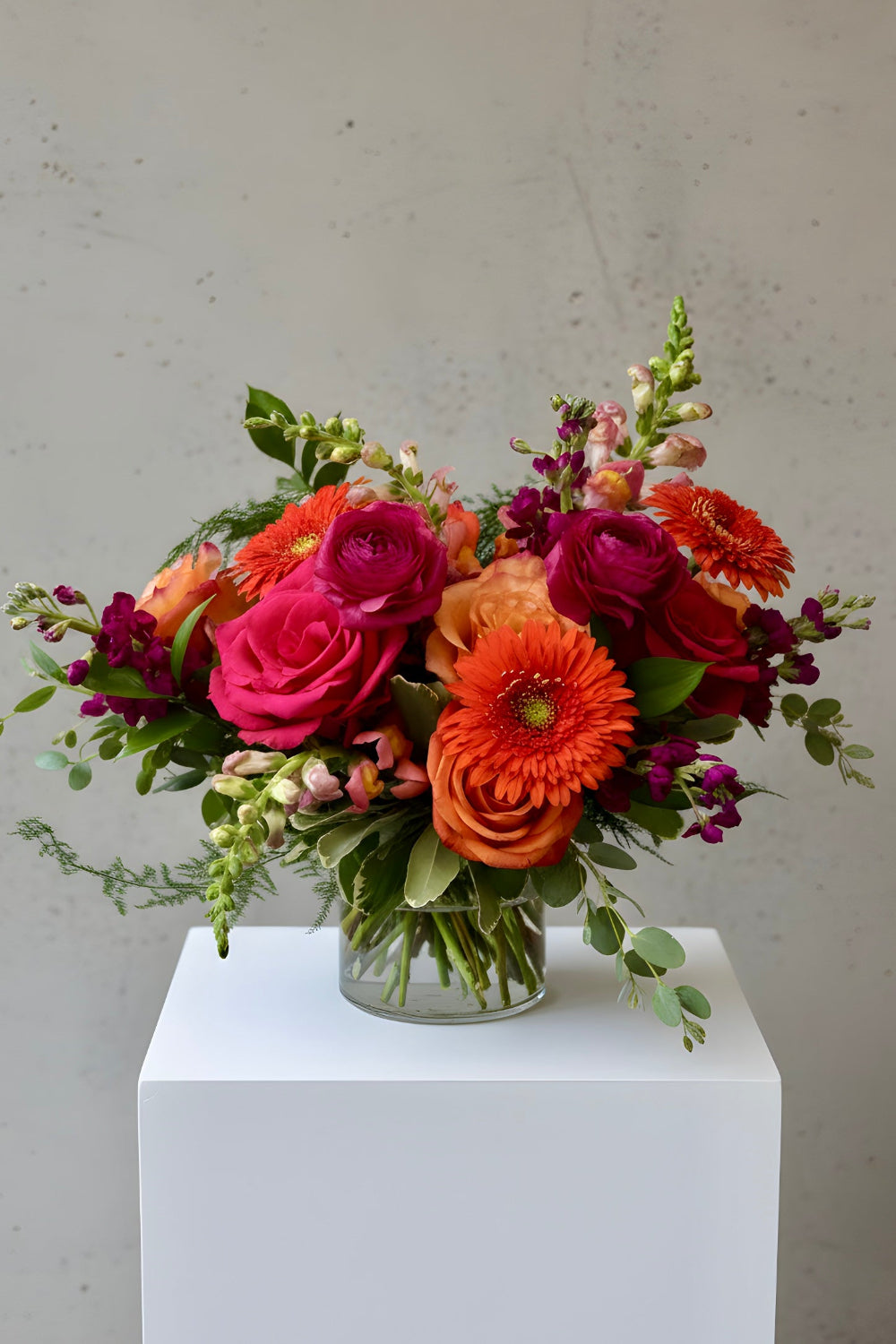 bouquet of oranges and hot pinks with roses, snapdragons, gerbera daisies, stock and ranunculus designed in a glass vase