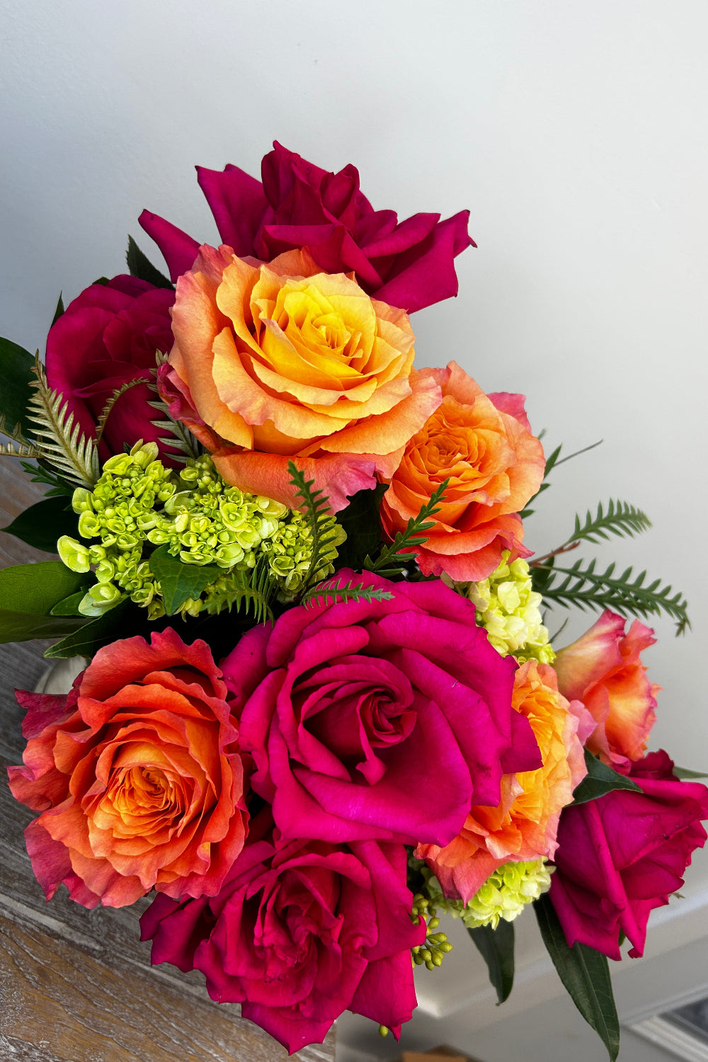 Detail shot of Sunset Spark bouquet featuring vibrant hot pink and coral roses with green hydrangea, highlighting modern floral design and fresh, high‑quality flowers.