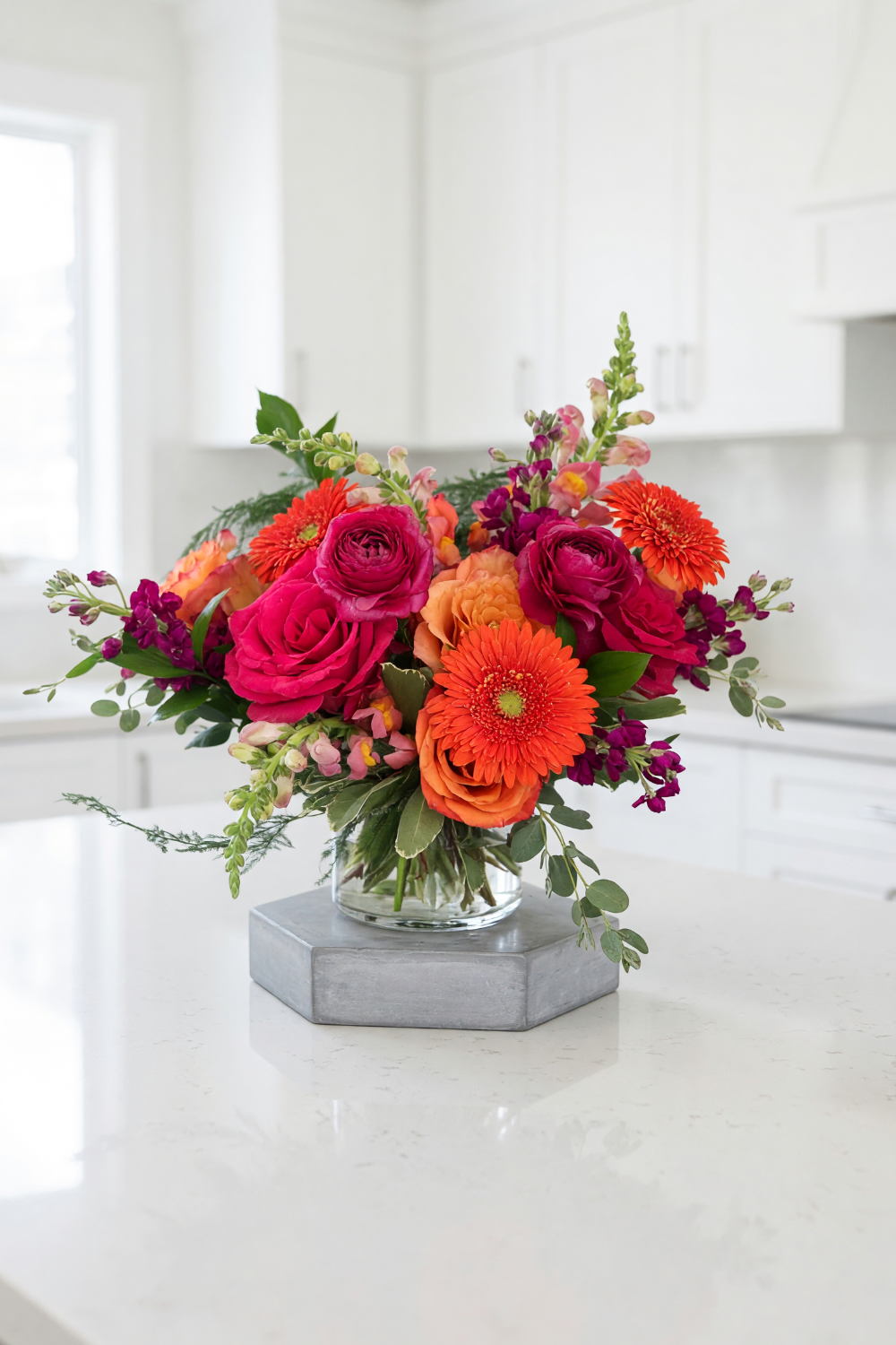 bouquet of hot pink and orange flowers designed on a vase displayed on a kitchen island